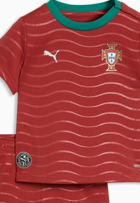 Set composto da maglia sportiva rossa e pantaloncini con motivo ondulato, colletto verde, logo Puma ed emblema della nazionale portoghese sul petto.