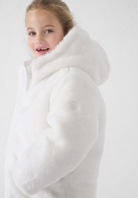 Chaqueta de piel sintética blanca con una gran capucha, cremallera frontal y textura suave. Cuenta con un parche de logo en el brazo izquierdo.