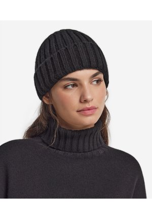 Kvinde iført en sort ribstrikket beanie og matchende sort ribstrikket rullekravesweater, der kigger let til højre.