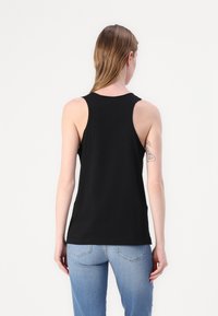 Μαύρη αμάνικη μπλούζα με στρογγυλή λαιμόκοψη και ίσιο στρίφωμα, συνδυασμένη με ανοιχτό μπλε τζιν. Απαλή υφή, ελάχιστος σχεδιασμός, χωρίς μοτίβα.