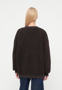 Sudadera marrón de forro polar con ajuste holgado, cuello redondo y puños acanalados. Cuenta con una superficie texturizada y dobladillo elástico.