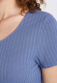 Haut en maille texturée bleue avec des côtes horizontales, un décolleté en V et des manches courtes. Le tissu a un léger lustre et une finition lisse.