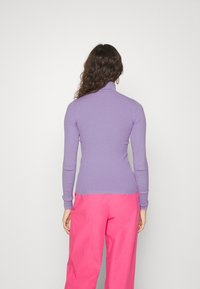 Lila ribbad polotröja, lång ärm, slim fit, kombinerad med klara rosa byxor. Slät textur, minimalistisk design utan synliga knäppningar.