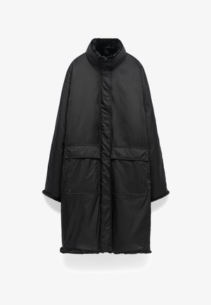 Zwarte lange gewatteerde jas met hoge kraag, twee grote voorzakken met klep en een zachte voering zichtbaar bij de manchetten en kraag.