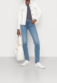 White denim jacket, navy and white striped shirt, light blue jeans, white sneakers, and cream tote bag. All items on a neutral background.
