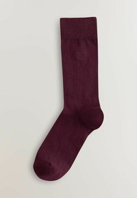 Calzino viola scuro singolo con bordo a coste e piccolo logo quadrato ricamato nella parte superiore, posato su una superficie chiara.