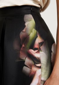 Gonna nera con stampa floreale nei toni del rosa e del verde. Realizzata in tessuto texturizzato con pences laterali e dettaglio di chiusura con zip.