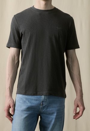 Ciemnoszary bawełniany t-shirt z krótkim rękawem i okrągłym dekoltem. Na lewej piersi znajduje się małe logo, a krój jest luźny. Zestawiony z niebieskimi jeansami.