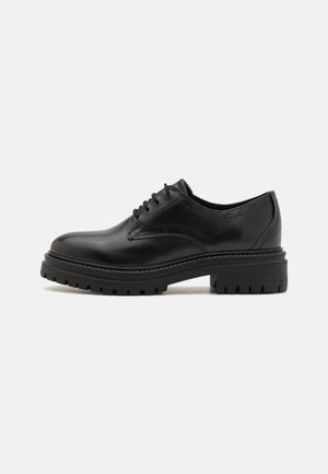 Scarpa oxford in pelle nera con finitura liscia, design con lacci e suola in gomma spessa caratterizzata da un motivo battistrada testurizzato.