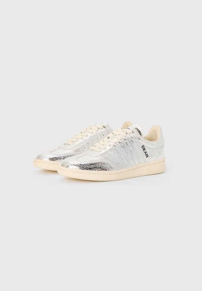 Silver sneakers with a cracked metallic finish, beige laces, and a textured design. Features branding on the side and a cream rubber sole.