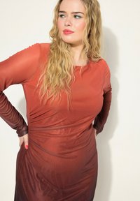 Pitkähihainen, vartalonmyötäinen mekko gradienssiväreissä punaisena, jossa on sileä, joustava kangas ja hienovaraisia rypytysdetaljeja sivuilla.