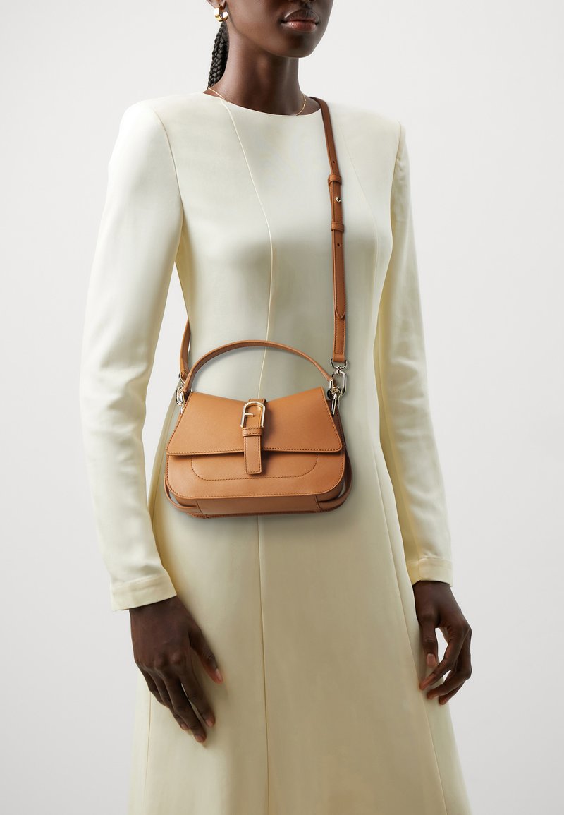Tan leather handbag with a structured shape, featuring a top handle, a detachable shoulder strap, and a front flap with a belt-like closure.