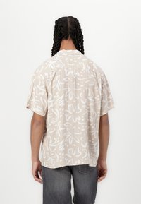 Kortermet beige skjorte med hvitt blomsterabstrakt mønster, lett stoff, avslappet passform og ryggklaffdetalj.