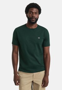 Tricou verde cu mâneci scurte, realizat din bumbac moale, având un guler rotund și un mic logo brodat pe piept.