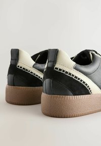 Schwarze und graue Sneakers mit einem Obermaterial aus strukturiertem Leder, kontrastierenden Creme-Akzenten, einem subtilen Stichdetail und einer Sohle aus Gummirubber.