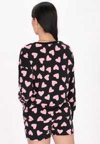 Svart pyjamasset med rosa hjärtmönster. Långärmad topp och shorts, tillverkad av mjukt tyg. Ribbad halsringning och manschetter.