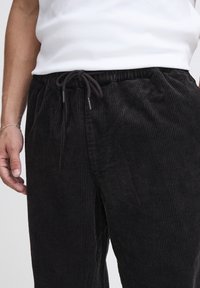 Pantaloni in velluto a coste neri con superficie testurizzata a coste. Presentano una cintura elasticizzata con coulisse per una vestibilità regolabile.