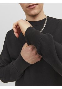 Felpa nera in cotone, con maniche lunghe e polsini a costine. Una collana a catena d'argento aggiunge un dettaglio a contrasto.