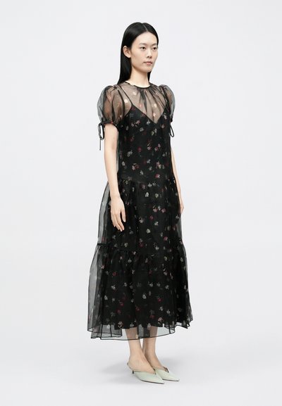 Rochie midi neagră cu imprimeu floral, mâneci bufante transparente, design în straturi și șnururi la mâneci. Are un model floral pe un material ușor.