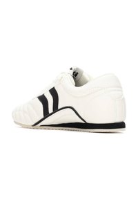 Zapatillas de cuero blanco con franjas negras, de perfil bajo, con cuello acolchado, superficie texturizada y suela de goma para mayor agarre.