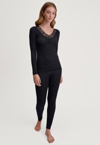 Zwart long-sleeve top met een V-hals en kantafwerking, gecombineerd met bijpassende zwarte leggings, beide gemaakt van zachte, rekbare stof.