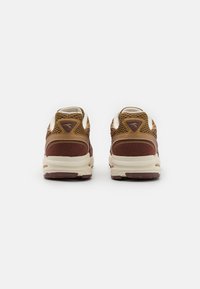 Zapatillas deportivas marrones y beige con paneles de malla, suelas de goma y un acabado texturizado. La vista trasera muestra el logo en el talón y un collar acolchado.