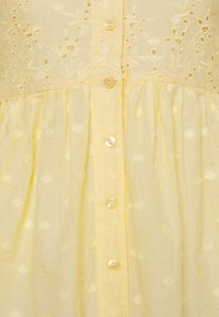 Gelbes Baumwollkleid mit bestickten Blumendetails, Knopfleiste vorne und plissiertem Rock mit einem dezenten strukturierten Muster.