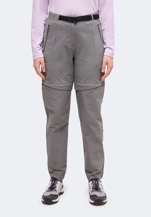 Personne portant un pantalon convertible gris clair avec jambes zippées, ceinture noire, chemise à manches longues lavande claire et baskets grises et blanches.
