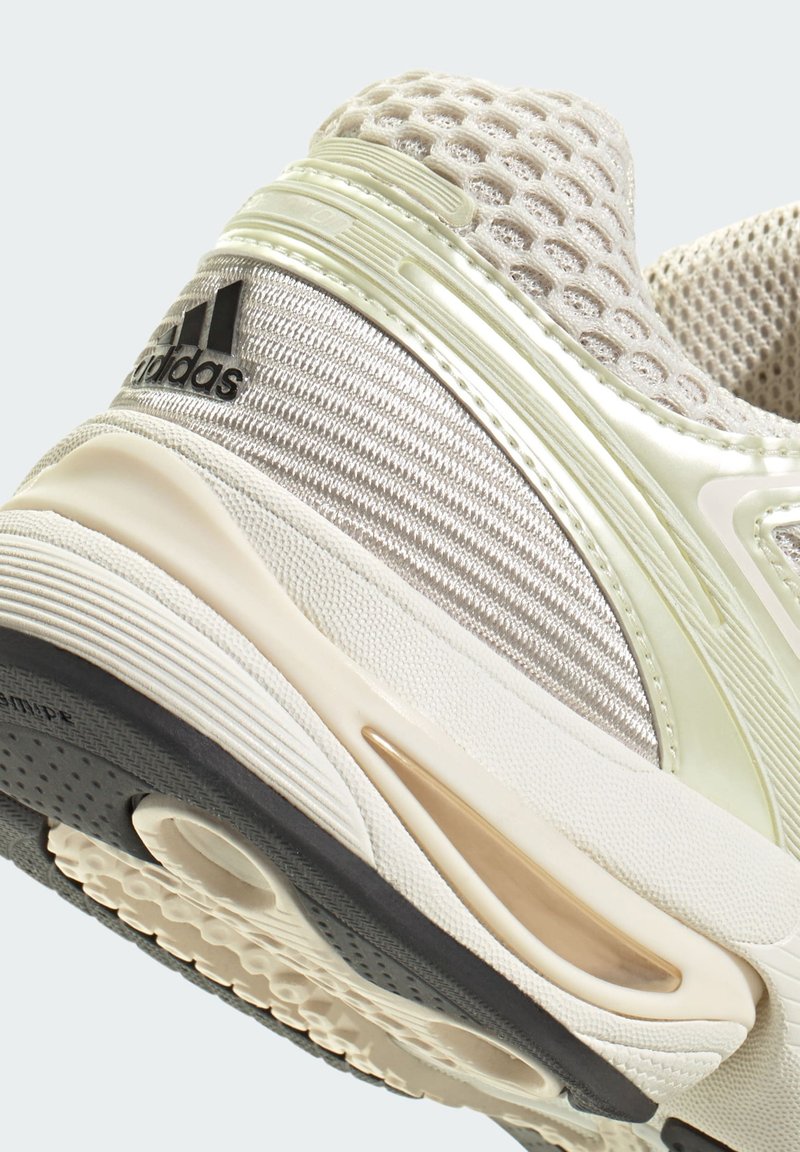 Helle Sportschuhe mit Obermaterial aus Mesh, strukturierten silbernen Akzenten, Gummisohle und markantem schwarzen Adidas-Logo. Leicht geschwungenes Design.