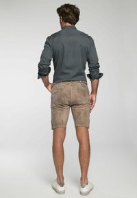 Hombre visto desde atrás que lleva una camisa texturada de color azul oscuro con un patrón sutil y pantalones cortos de color marrón claro. El calzado es blanco con acentos grises.