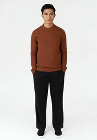 Brun ribbestrikket genser, svarte vide bukser og svarte joggesko. Enkel, moderne design med rund hals.
