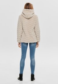 Beżowa kurtka z sztucznego futra z kapturem, w deseń w zygzaki. Założona z niebieskimi obcisłymi dżinsami i czarnymi botkami do kostek.