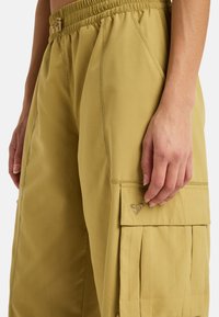 Pantaloni cargo in khaki tenue, con una texture morbida, vita elastica, tasche laterali e un logo a cuore ricamato sulla tasca cargo.