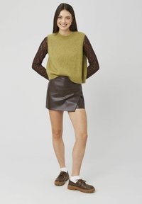 Pull en tricot vert olive avec manches longues en dentelle, associé à une mini-jupe en cuir marron brillant et des chaussures marron avec des chaussettes blanches.