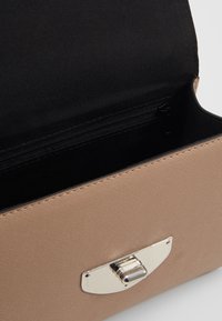 Beżowa torebka o gładkiej fakturze, zapięcie na srebrny metalowy zatrzask. Wnętrze wyłożone czarną tkaniną, widoczna kieszeń na suwak.