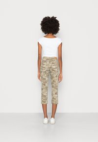 Top branco de mangas curtas, ajustado, combinado com calças de camuflagem cropped em tons de bege, tecido texturizado, e ténis brancos com marcação na lateral.