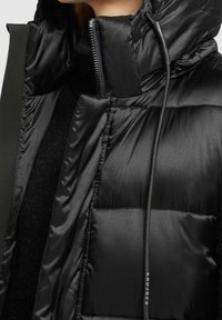 Czarna kurtka puchowa z błyszczącego, pikowanego materiału, z wysokim kołnierzem i zamkiem błyskawicznym z sznurkiem, prezentująca nowoczesny, elegancki design.