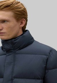 Chaqueta acolchada en color marino con cuello alto, diseño acolchado y textura suave. Incluye un cierre con cremallera y detalles mínimos.