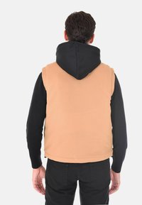 Gilet beige con superficie testurizzata, abbinato a una felpa nera con cappuccio. Presenta una vestibilità regolare e un design a strati. Tessuto semplice, senza fantasie.