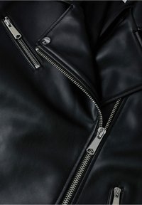 Veste en cuir noir avec fermetures éclair argentées, détails à boutons-pression et finition texturée. Poches zippées remarquables à l'avant et col triangulaire.