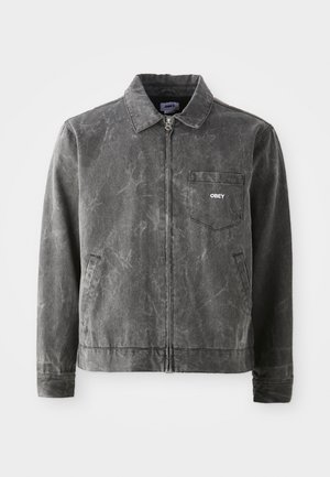 Gray canvas jacket with a collar, front zip closure, and a left chest pocket. It features a subtle textured finish and side pockets.