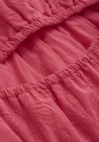 Tessuto rosa pallido con un motivo floreale testurizzato e dettagli in elastico arricciato. Materiale morbido e leggero con una finitura liscia.
