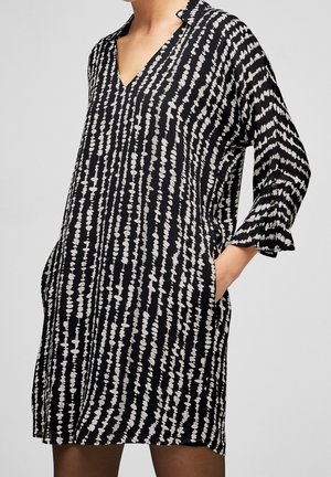 Robe imprimée noir et blanc avec un décolleté en V, des manches trois-quarts et des poignets évasés. Présente une coupe ample et des poches latérales.