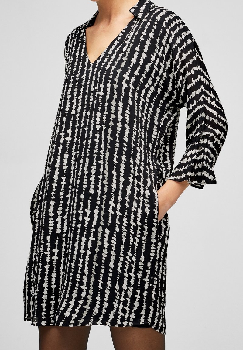 Svart och vit mönstrad klänning med V-ringning, trekvartsärmar och utsvängda manschetter. Har en lös passform och sidofickor.