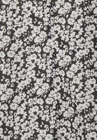 Tessuto nero con un motivo floreale bianco, caratterizzato da piccoli fiori e foglie. Leggera texture e un dettaglio di cucitura visibile.