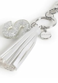 Llavero con un charm claro y brillante en forma de "S", con un borlón de cuero blanco y herrajes plateados, además de una etiqueta circular con la palabra "MIRIAD" grabada.