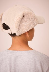 Kasket med en beige uldkrop og fluffy beige øreflapper; justerbar rem bagpå; blødt, tekstureret materiale.