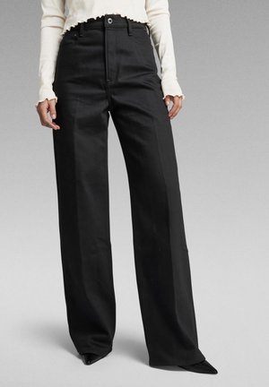Pantalones negros de pierna ancha con cintura alta, hechos de una tela suave. Presentan bolsillos laterales, trabillas para el cinturón y un ajuste entallado.