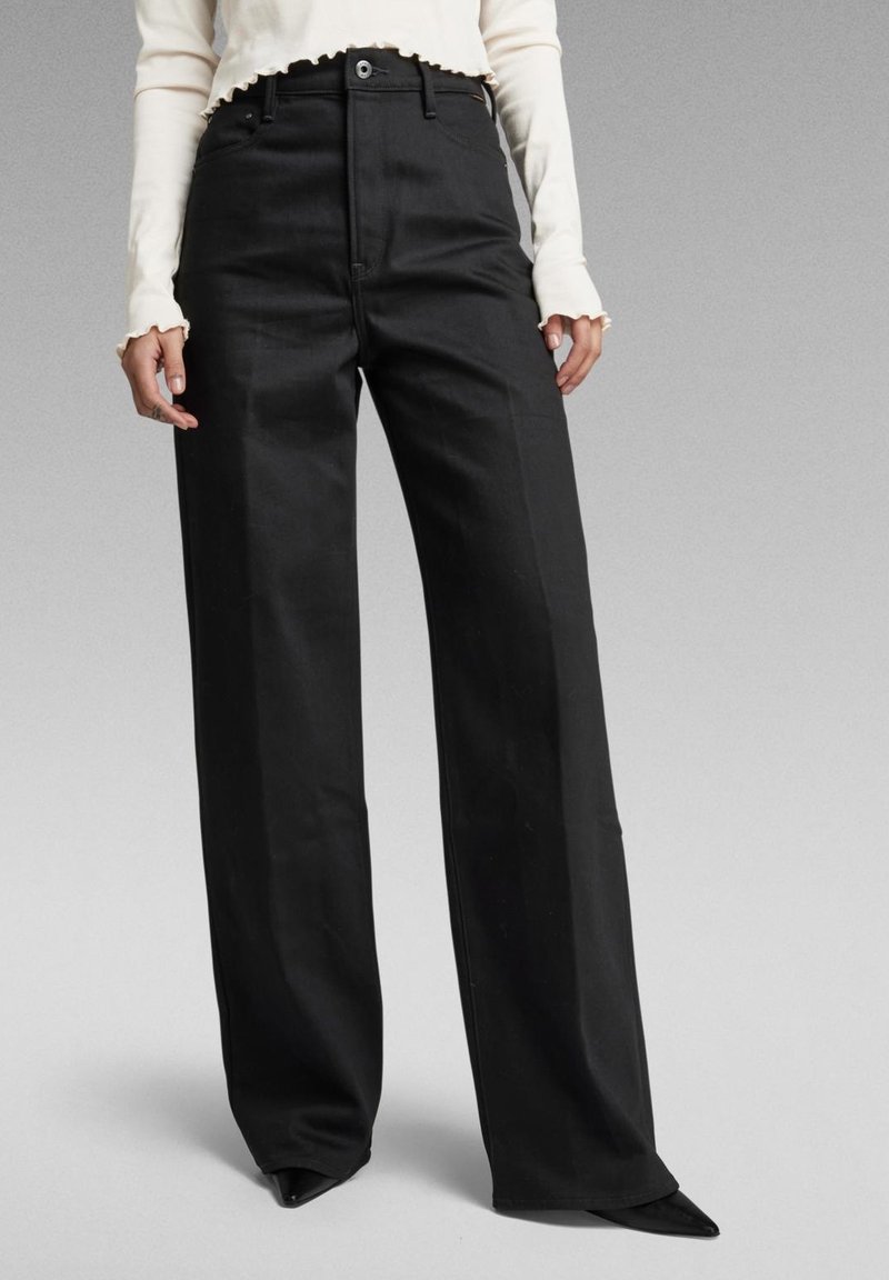 Svarta vida byxor med hög midja, tillverkade av ett mjukt tyg. Har sidofickor, bälteshällor och en skräddarsydd passform.