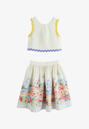 Haut sans manches crème avec bordure jaune et violette, assorti à une jupe aux imprimés colorés représentant une ville côtière et des motifs floraux.